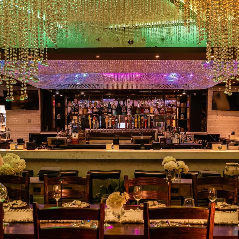 Elegant restaurant dining room with a fully stocked bar, crystal bead ceiling decor, set tables, floral arrangements, and warm ambient lighting.