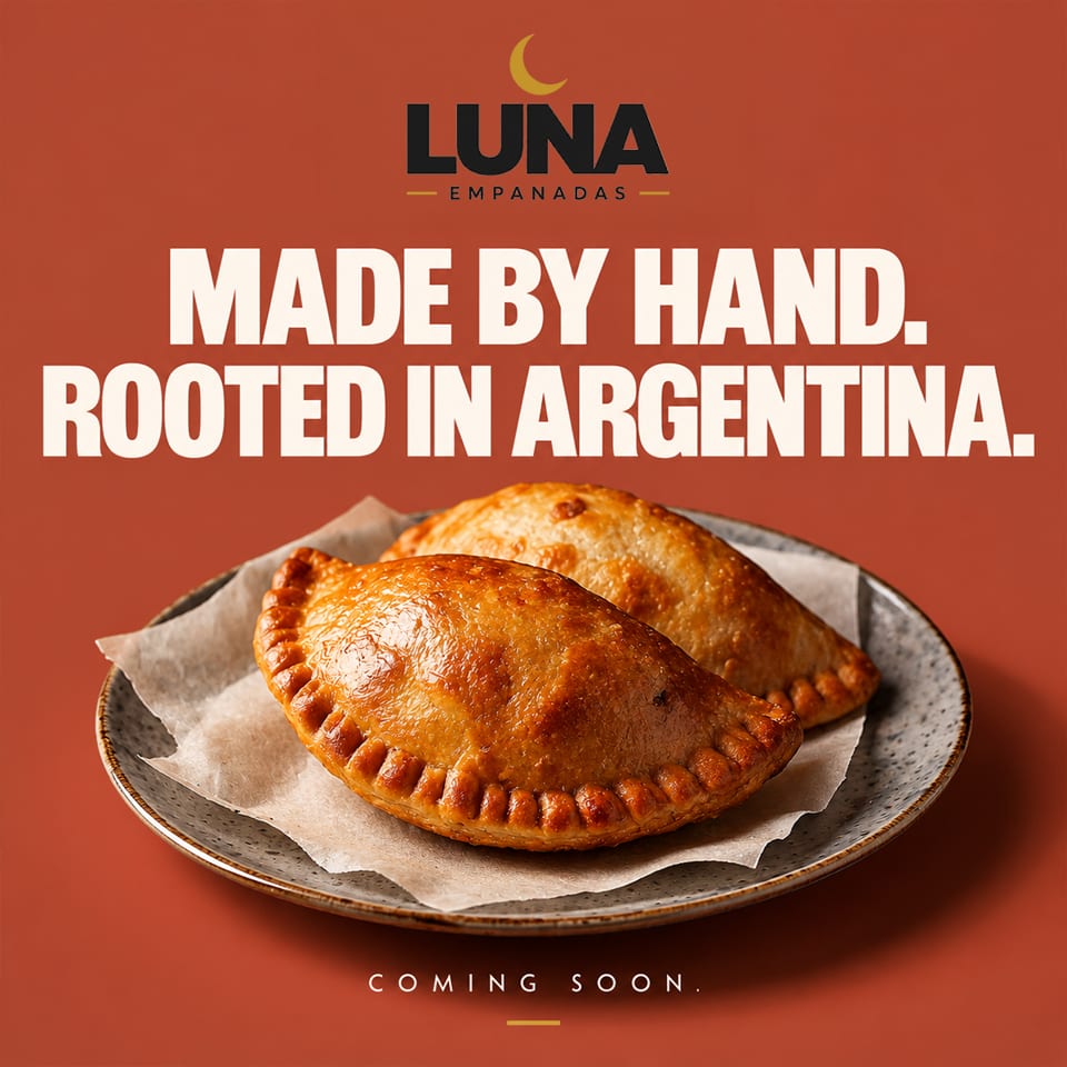 Two golden-brown empanadas sit on parchment-lined ceramic plate beneath Luna Empanadas branding and “Made by hand” text.