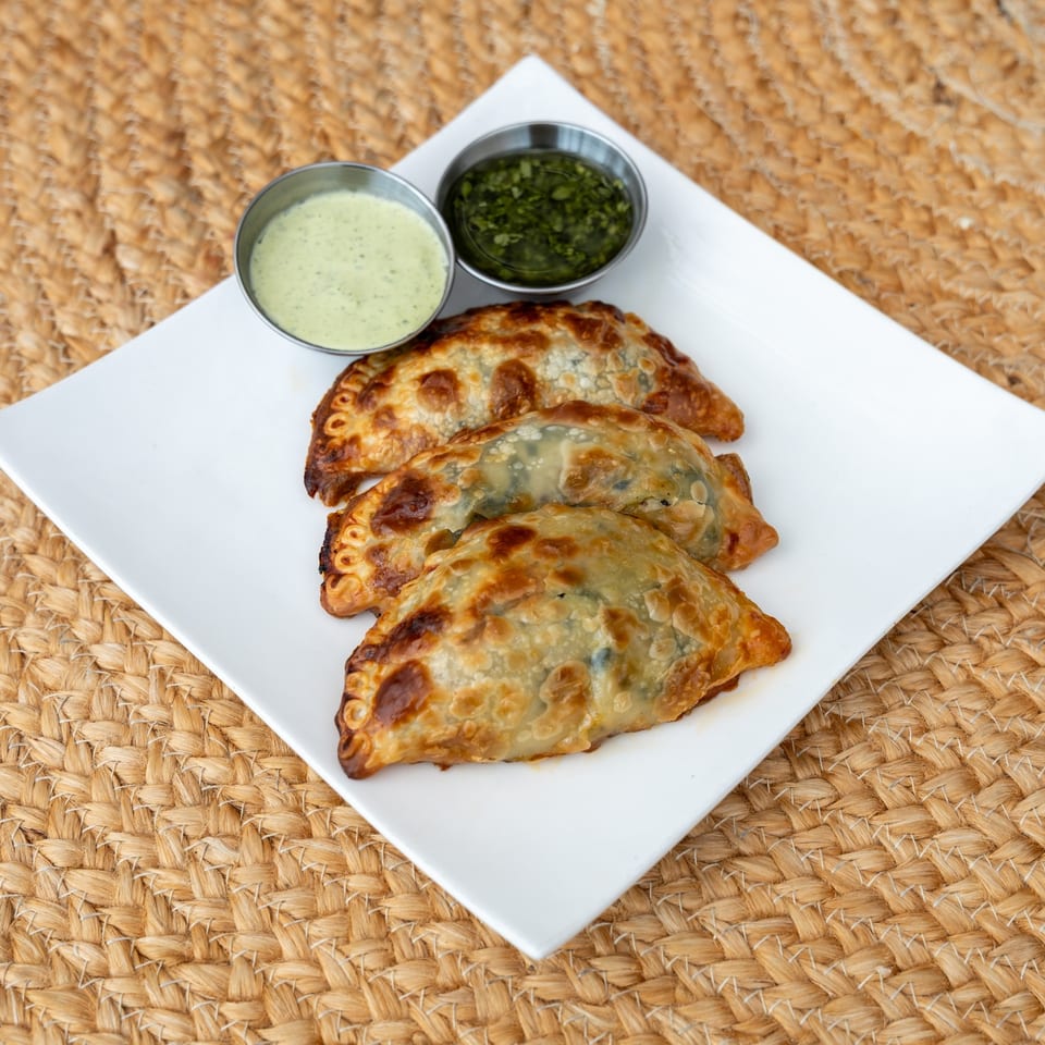 Spinach and ricotta empanadas broken open beside chimichurri and green sauce.
