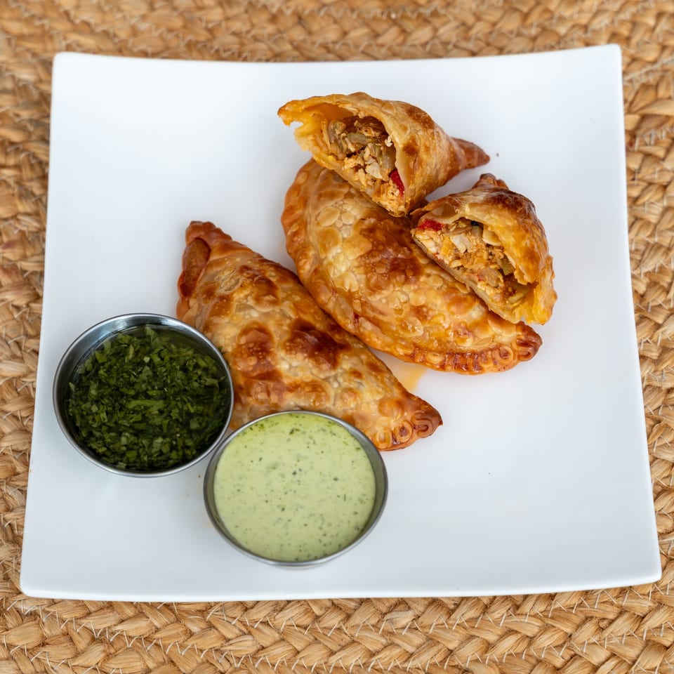 Chicken empanadas with a golden, blistered crust and two green sauces.