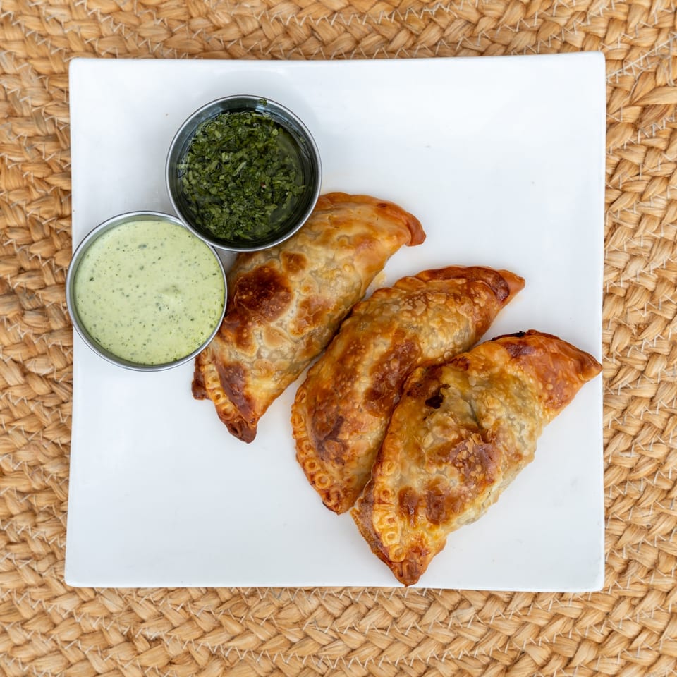 Three golden-baked Argentine beef empanadas with chimichurri and creamy green garlic sauce.