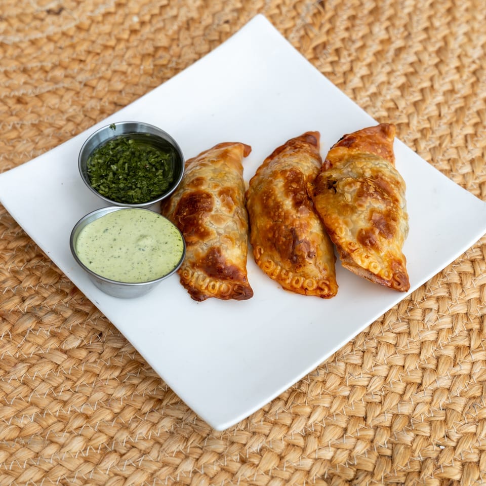 Baked beef empanadas with crimped edges alongside two dipping sauces.